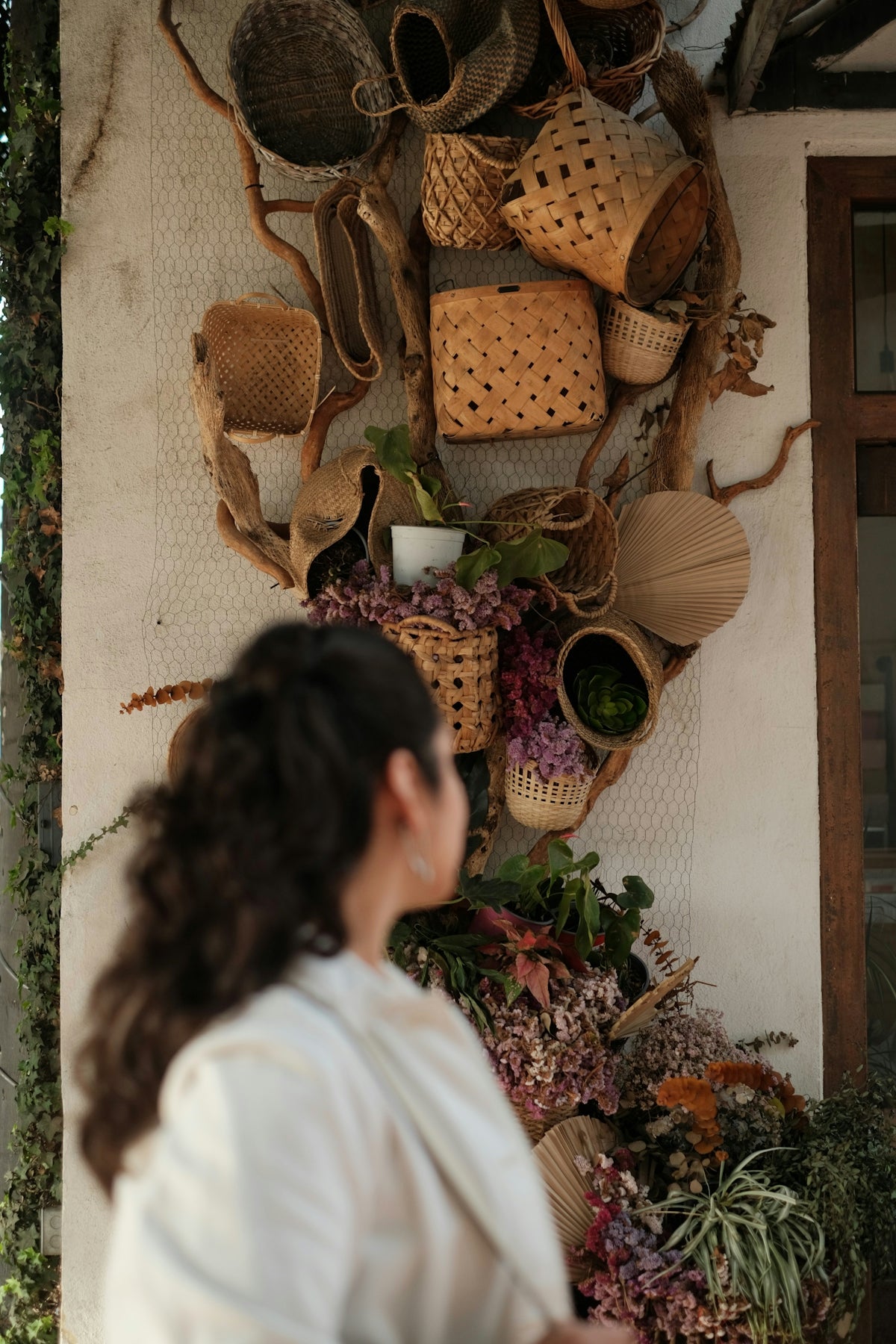 Woman admiring a wall decorated with woven baskets and plants.